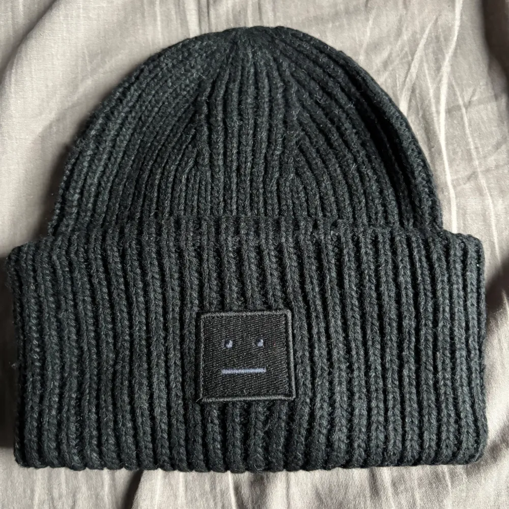 Säljer en snygg svart ribbad mössa från Acne Studios. Den är i nytt skick och har en stilren design med en liten fyrkantig patch framtill. Perfekt för höst och vinter för att hålla dig varm och trendig.. Accessoarer.