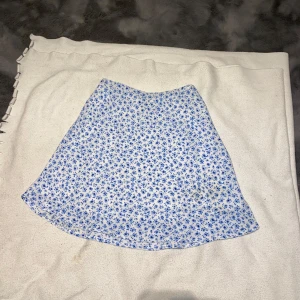 Blommig kjol från Divided - Söt blommig kjol från Divided i vitt med blå blommor. Perfekt för sommardagar eller en avslappnad vårlook. Kjolen har en bekväm passform och är i mycket bra skick. Den är lätt och luftig, vilket gör den idealisk för varmare väder. Pris kan diskuteras 