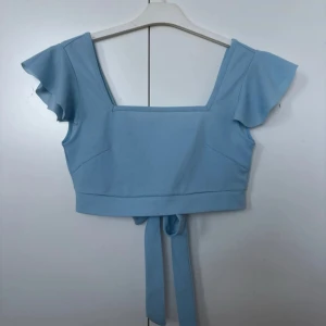 Ljusblå topp med volangärmar - Säljer en superfin ljusblå topp med volangärmar och knytning i ryggen. Super snygg till sommarn, endast använd en gång!