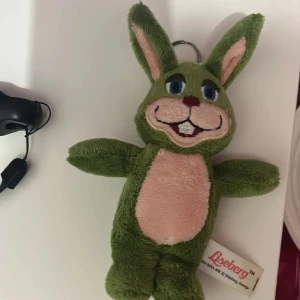 Reserverad lisse - En söt grön kaninmjukis från Liseberg med rosa detaljer på magen och öronen. Den har ett glatt ansikte och en nyckelring för att fästa på väskor eller nycklar. Perfekt som en liten present eller souvenir från Liseberg.