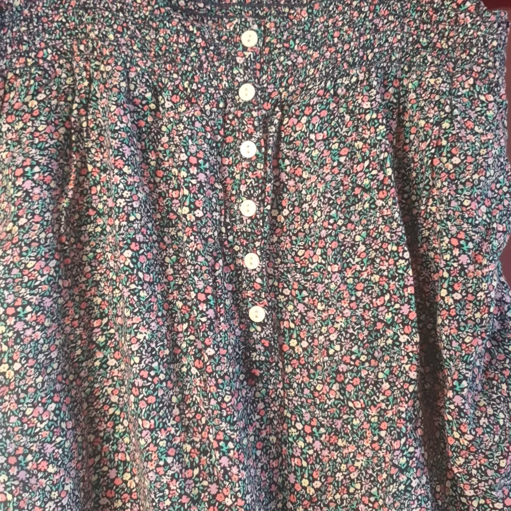 Söt blommig jympsuit i mörkblått med små rosa och vita blommor. Den har knappar framtill och en bekväm passform. Perfekt för vår och sommar! 🌸. Shorts.