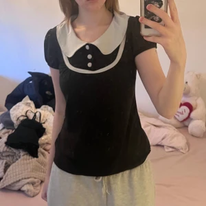 Svart topp med vit krage och knappar - Säljer en söt svart topp med en stor vit krage och dekorativa knappar framtill. skriv för frågor