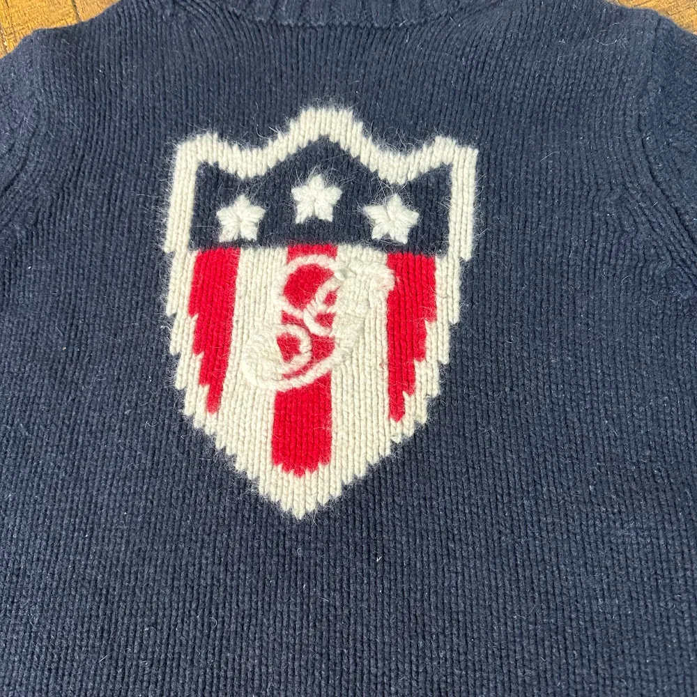 Säljer en snygg mörkblå stickad polotröja från GANT med ett coolt emblem i rött och vitt på framsidan. Tröjan har en hög krage och långa ärmar, perfekt för kyliga dagar. Den är i mycket bra skick och supermysig att ha på sig. Passar perfekt till både vardag och lite finare tillfällen. 🧥✨. Tröjor & Koftor.