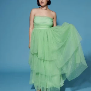 Grön axelbandslös klänning - Säljer en fantastisk grön axelbandslös klänning i lager-på-lager stil. Perfekt för fest eller bal. Klänningen har en luftig och elegant design som ger en drömlik känsla. Den är i mycket bra skick och passar perfekt för en speciell kväll.