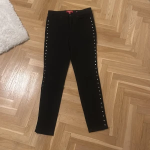 Svarta jeans med nitar från Guess - Snygga svarta jeans från Guess med coola nitar längs sidorna. De är högmidjade och har en slim passform som sitter perfekt. Perfekta för en utekväll eller när du vill känna dig extra stylish. De är i mycket bra skick och redo för nya äventyr!