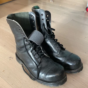 Svarta kängor med snörning (DR MARTIN) - Säljer ett par svarta kängor i bra skick. De har en robust design med snörning och är perfekta för höst och vinter. Kängorna är gjorda av skinn och har en slitstark sula, vilket gör dem idealiska för utomhusaktiviteter. 