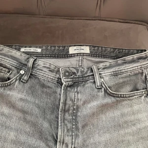 Grå jeans från Jack & Jones - Säljer ett par grå jeans från Jack & Jones i storlek 31/34. De har en relaxed fit och är perfekta för en casual look. Jeansen har en klassisk femficksdesign och är i mycket bra skick. Perfekta för både vardag och fest!