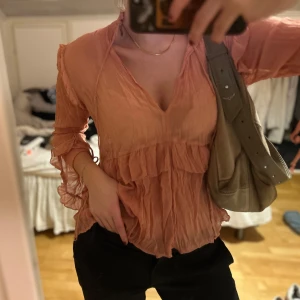 Rosa blus med volanger - Säljer en superfin rosa blus med volanger och v-ringning. Den har långa ärmar med knytning och volangdetaljer.