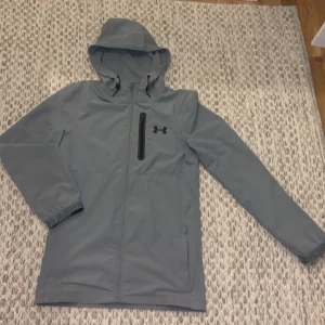 Under armour  - Säljer en grå vindjacka från Under Armour i mycket bra skick. Jackan är använd typ 1 månad utan någon fläcka eller skada. 