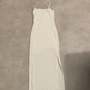 Vit långklänning från Bershka - Säljer en superfin vit långklänning från Bershka i storlek S. Den är helt oanvänd och säljer för den tyvärr inte passar. Denna klänningen säljs inte längre på deras hemsida. Klänningen har smala axelband och en stilren slits på sidan. Perfekt för sommarens alla fester eller en dag på stranden. Materialet är lätt och bekvämt, vilket gör den idealisk för varma dagar. 🌞