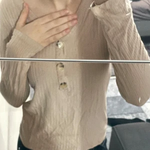Beige ribbad tröja med knappar - Säljer en snygg beige ribbad tröja med knappar framtill. Den har en tight passform och långa ärmar. Den är använd men väl tagen hand om.