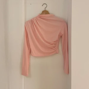 Rosa långärmad topp - Säljer en söt rosa långärmad topp i ett mjukt och stretchigt material. Toppen har en unik drapering på ena sidan som ger en snygg detalj. Perfekt för både vardag och fest!