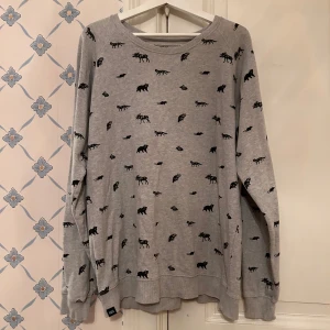 Grå tröja med djurmönster - Säljer en grå tröja med ett coolt djurmönster i svart. Tröjan har långa ärmar och en avslappnad passform, perfekt för mysiga dagar. Den är i bra skick och passar perfekt till både vardag och chill.