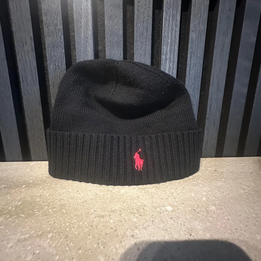 Snygg svart mössa från Polo Ralph Lauren i stickat material. Den har en röd broderad logga framtill och är i one size. Perfekt för att hålla sig varm och stilren under kyliga dagar. Är i jätte bra skick!🥰. Accessoarer.