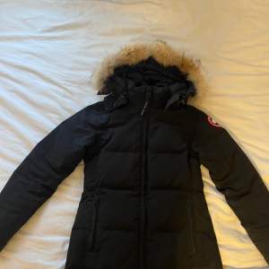 Säljer en svart dunjacka från Canada Goose. Jackan har en mysig pälsdetalj på huvan och dragkedja framtill. Perfekt för kalla vinterdagar. Den är långärmad och har en klassisk passform. Supervarm och stilren! Jackan är lite missfärgad på armarna utöver de så är den i bra skick. Priset går att diskutera 