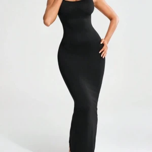 Svart tight klänning - Snygg svart tight klänning som framhäver dina naturliga kurvor. Den har en slits och är perfekt för både fest och vardag. Kan bäras ensam eller som ett lager för extra stil. Klänningen har en smickrande passform med magkontroll för en slimmad look.