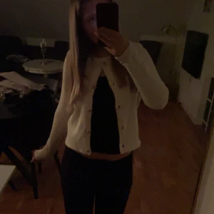 Vit kofta med knappar - Säljer en stilren vit kofta med knappar framtill. Perfekt för både vardag och festliga tillfällen. Koftan har en normal passform och är långärmad, vilket gör den idealisk för kyligare dagar. Ett måste i garderoben för alla säsonger!