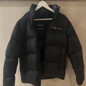 Svart dunjacka från sail raicing - Säljer en svart dunjacka från sail raicing i mycket bra skick. Jackan är perfekt för vintern med sin pufferstil och långa ärmar. Den har en dragkedja framtill och en mysig huva för extra värme. Superstylish och håller dig varm hela säsongen!   Nypris 3100kr   Skick 10/10