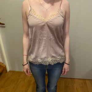 Beige sidenlinne med spetsdetaljer - Säljer ett elegant beige linne i siden med vacker spets längs halsringningen och nederkanten. Perfekt för en somrig dag eller en festlig kväll. Linnet har justerbara axelband för bästa passform. Superfint och bekvämt! 🌟