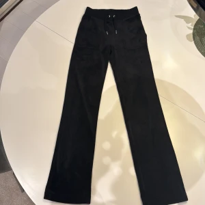 Svarta mjukisbyxor från Juicy Couture - Säljer ett par svarta mjukisbyxor från Juicy Couture i storlek XXS. Byxorna har en bekväm passform med snörning i midjan och fickor både fram och bak. Långa i benen. Passar mig perfekt och är till och med lite långa på mig som är 165 cm . Använda men mycket bra skick, inga defekter😍