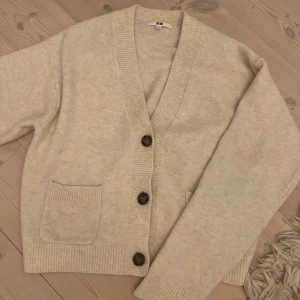 Beige kofta från Uniqlo - Mysig beige kofta från Uniqlo i ett mjukt material. Den har en v-ringad design med stora knappar och två fickor framtill. Passar till både vardag och mysiga hemmakvällar. Helt oanvänd och är i topp skick. Nypris 449, säljer för 350🥰🥰