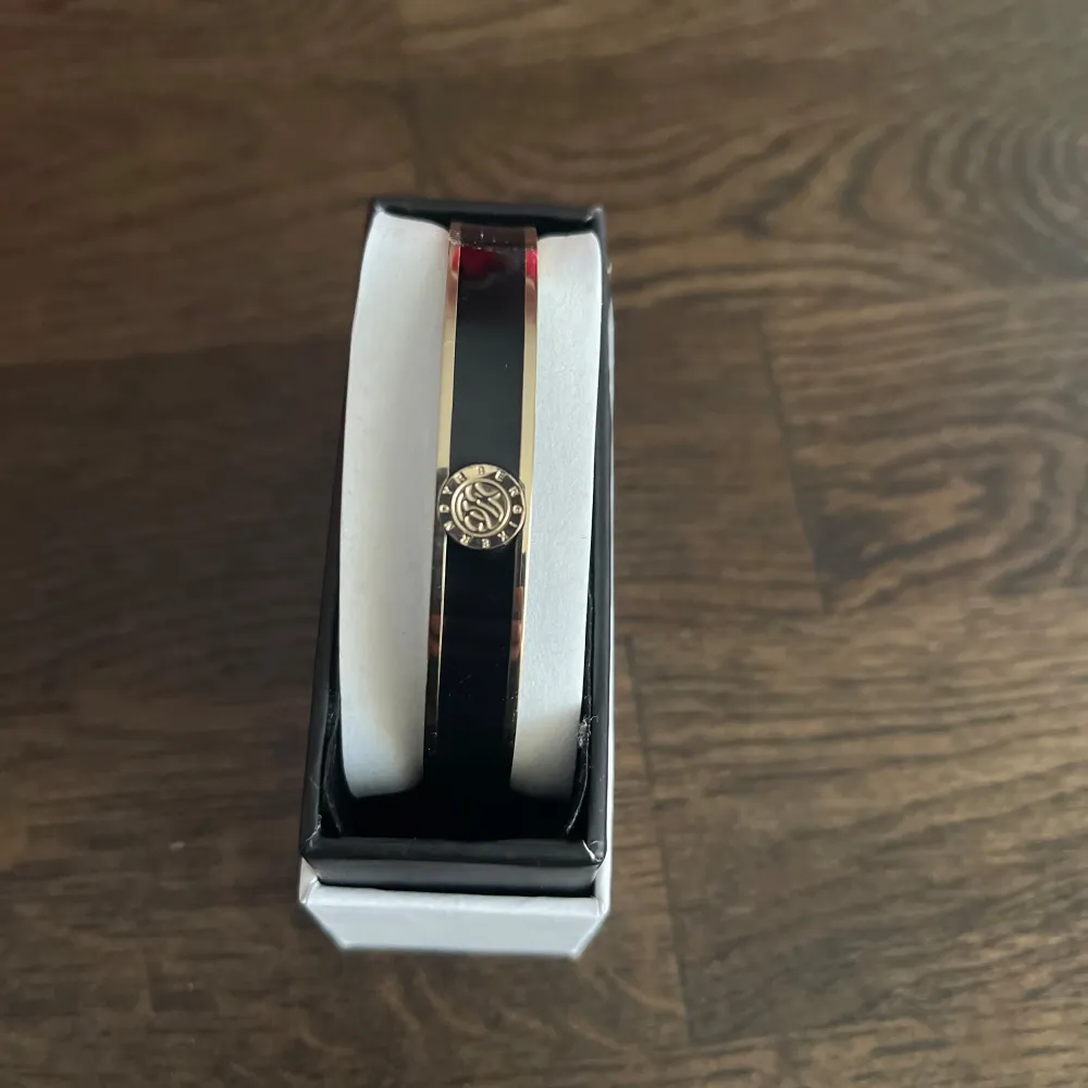 Snyggt armband i svart och guld med en elegant rund detalj i mitten. Perfekt för att ge en touch av stil till vilken outfit som helst. Armbandet har en slät och glansig yta som ger en lyxig känsla. Kommer i en fin förpackning, redo att ges bort som present eller att användas direkt.. Accessoarer.