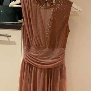 Tävlingsdräkt - En vacker tävlingsdräkt med glittrande detaljer. Dräkten har en rund halsringning och en öppen rygg. Den är gjord av ett tunt, genomskinligt tyg och har en kjol. Helt ny, aldrig använd med prislappen kvar.