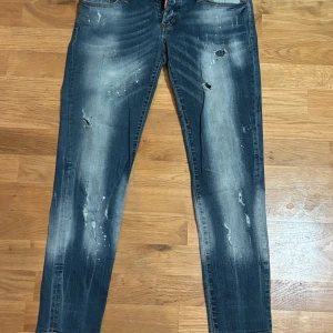Blå jeans från Dsquared2 - Säljer ett par snygga blå jeans från Dsquared2 i storlek 44 . Perfekta jeans med slitna detaljer och en cool tvätt. De har en knappgylf och klassiska femficksdesign. Perfekta för en avslappnad stil med en touch av edge. Passar både till vardags och fest!