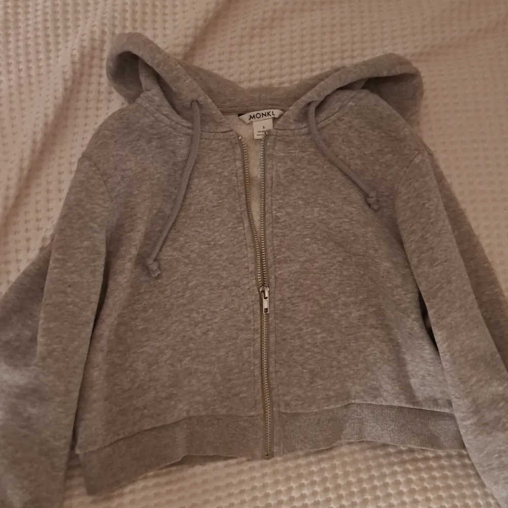 Säljer en grå croppad hoodie från Monki i storlek S. Den har dragkedja och huva med snören, perfekt som en liten extra touch till sin outfit. Passar bra till både jeans och kjol. Använd  fåtal gånger så är i mycket bra skick. Perfekt för höst och vår!. Hoodies.