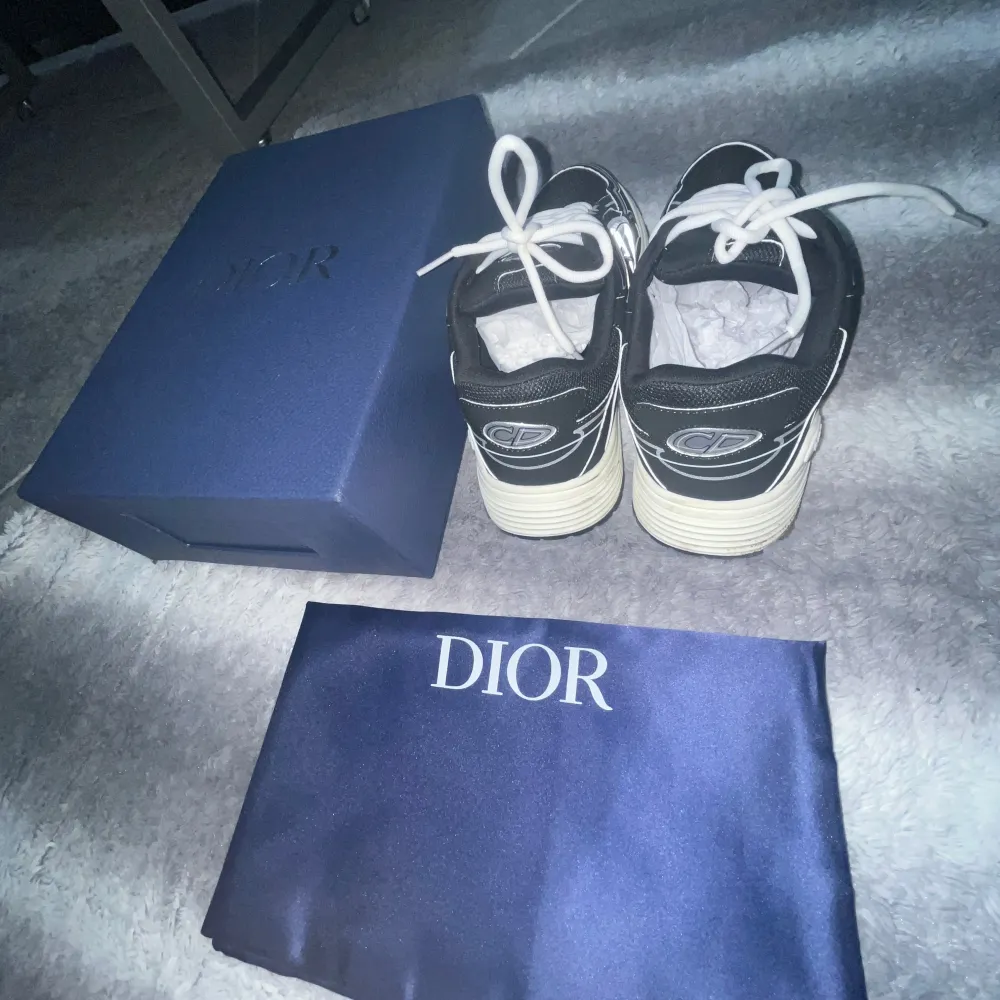 Säljer ett par snygga svarta dior sneakers i nytt skick. Skorna har en cool design med vita detaljer och snörning. De kommer i originalförpackning med en blå Dior-dustbag. Perfekta för att ge din outfit en lyxig touch! Säljer den eftersom jag gillar inte färgen. Pris kan diskuteras.. Skor.