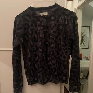 Svart leopardmönstrad kofta från Zadig & Voltaire - Säljer en supercool svart kofta från Zadig & Voltaire med leopardmönster och texten 'ROCK' i glittriga stenar på ryggen. Den har långa ärmar och knappar framtill. ❤️