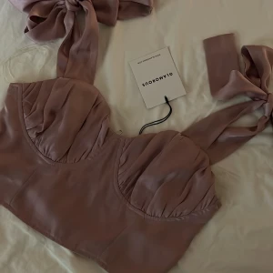 Lila korsettopp från Glamorous - Snygg lila korsettopp från Glamorous i storlek E. Toppen har en elegant design med knytband och dragkedja i sidan. Perfekt för festliga tillfällen!