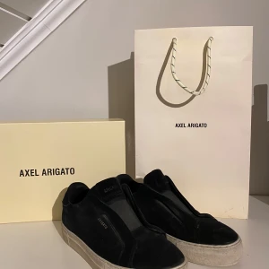 Svarta sneakers från Axel Arigato - Säljer ett par svarta sneakers från Axel Arigato i bra skick. De har en stilren design med en tjock vit sula och är tillverkade i mocka. Perfekta för både vardag och fest. Skorna kommer med originalförpackning och påse.