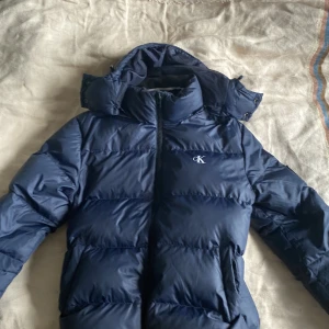 Mörkblå dunjacka från Calvin Klein Jeans - Säljer en calvin klein jacka som är i helt nytt skick förutom lite smuts på insidan av jackan som inte styns när den är på. 