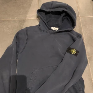 Stone Island hoodie - Tjaa säljer nu en stilren hoodie frå Stone Island i grymt skick🤩Storlek är 12-14 år och passar från 156-166. Den har en CLG kod inuti för att verifiera äktenskap💯✅ Perfekt för både vardag och chill och passar bra nu mot höst och vinter🍂❄️, ett måste i garderoben‼️Skriv för fler frågor eller funderingar🫡