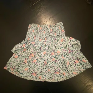 Blommig kjol från Vero Moda - Superfin blommig kjol från Vero Moda i storlek M. Den har ett elastiskt midjeband och volangdetaljer. Kommer ej till användning så säljer. Använd fåtal gånger.