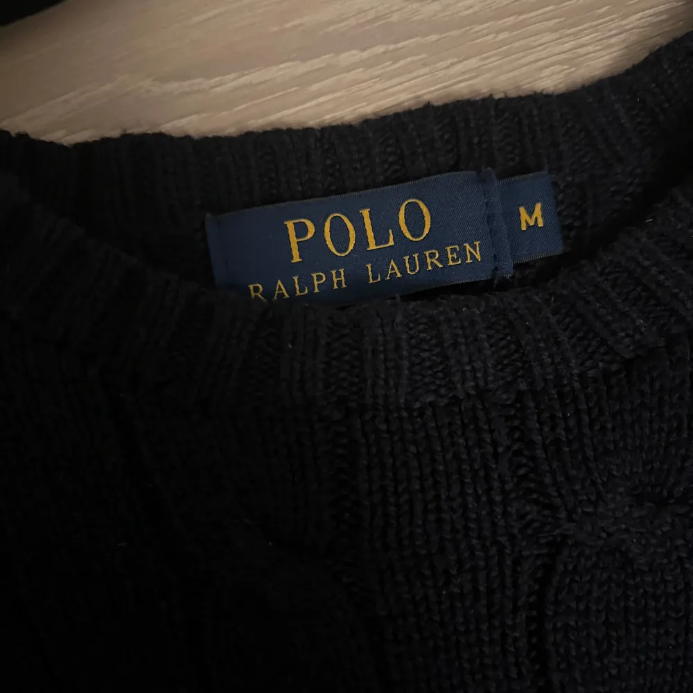 Säljer en snygg mörkblå stickad tröja från Polo Ralph Lauren. Den har ett klassiskt flätmönster och den ikoniska loggan broderad i orange på bröstet. Perfekt för höst och vinter, med långa ärmar och en bekväm passform. Passar både till vardags och lite finare tillfällen. Ny pris på denna ligger på ca 2500kr, mitt pris 1000kr!! Hör av er för fler bilder eller funderingar 😁. Tröjor & Koftor.