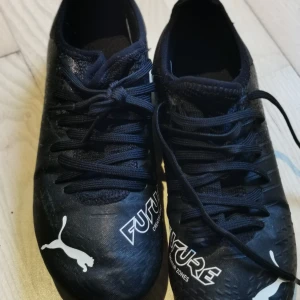 Svarta fotbollsskor från Puma - Säljer ett par svarta Puma Future fotbollsskor i bra skick. Skorna har snörning och är designade för optimal kontroll på planen. Perfekta för både träning och match. Storleken är 36.