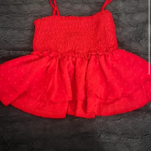 Röd ärmlös topp - Säljer en superfin röd ärmlös topp med smala axelband. Toppen har en smockad överdel och ett luftigt, volangigt fall nedtill. Perfekt för sommardagar eller en festlig kväll. Den är i mycket bra skick och redo för nya äventyr, är inte lika neon i värkligheten💕