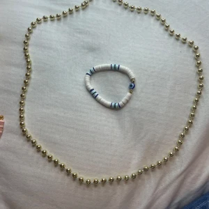  vitt armband med blå detaljer - Säljer ett trendigt vitt armband med blå och turkosa ränder. Armbandet har också en charm i form av ett blått öga. Perfekt för att ge din outfit en stilren touch!