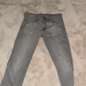 Grå Levis 511 jeans slim fit - Säljer ett par grå Levis 511 jeans i bra skick. De har en slim passform och är perfekta för både vardag och fest. Klassisk femficksdesign med dragkedja och knapp. Märkeslappen syns tydligt på baksidan. Passar perfekt till höst- och våroutfits! JEANSEN ÄR W34 MEN DEM MOTSVARAR W32. Jeansen är aldrig använda pga småa.
