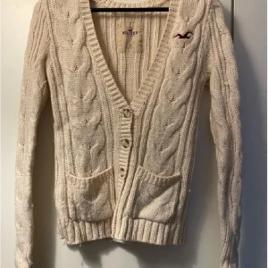 Beige stickad kofta från Hollister - Mysig beige stickad kofta från Hollister med flätmönster och knappar framtill. Den är köpt här på Plick men säljs då den inte kommer till så mycket användning. Den är jätte varm och i fint skick. Kom privat för fler bilder. XS men passar S🥰