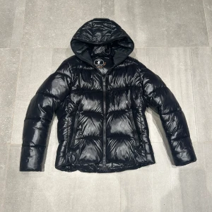 Svart pufferjacka från Save the Duck - Säljer en svart pufferjacka från Save the Duck i storlek M. Jackan är 100% animal free och har en glansig finish med dragkedja och huva. Perfekt för kalla dagar när du vill hålla dig varm och stilren. 🖤