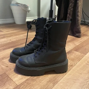 Svarta boots med snörning och dragkedja - Säljer ett par snygga svarta boots i skinn med både snörning och dragkedja på sidan. De har en rejäl sula som ger lite extra höjd och är perfekta för höst och vinter. 