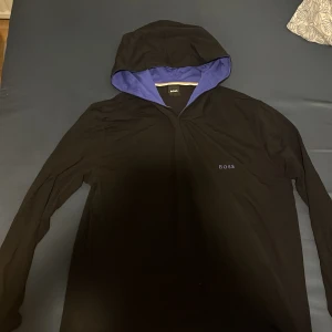 Svart hoodie från BOSS - Säljer en stilren svart hoodie från BOSS i storlek L. Den har en snygg lila insida på huvan och är perfekt för både vardag och chill. Hoodien är i bra skick och passar perfekt till höst och vår. Skön och enkel att matcha med det mesta! 🖤