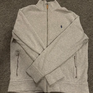 Grå zip-tröja från Ralph Lauren - Säljer en stilren grå zip-tröja från Ralph Lauren i storlek L. Tröjan har en dragkedja framtill och två praktiska fickor med dragkedja. Perfekt för både vardag och avslappnade tillfällen. Den är i mycket bra skick och superbekväm att ha på sig. Priset kan diskuteras, hör gärna av er vid frågor😊