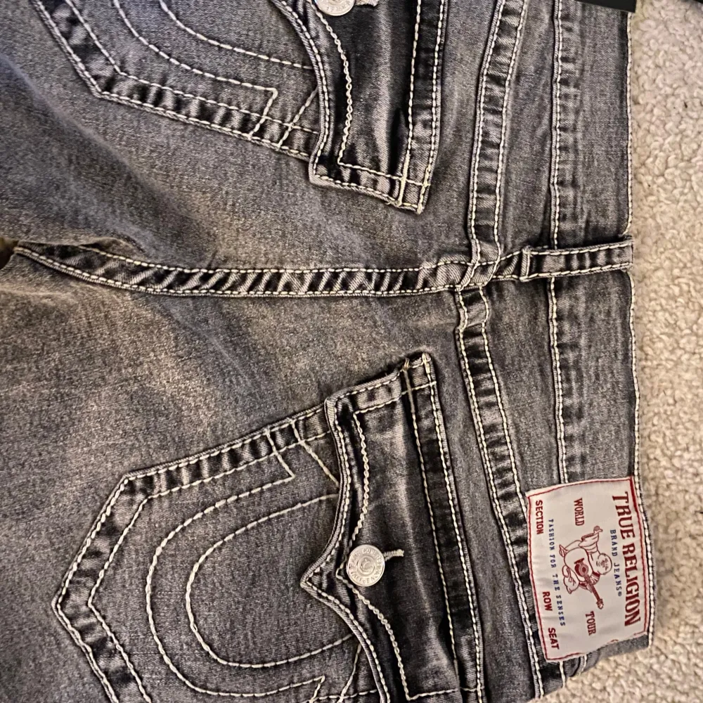 HELT NYA Säljer ett par grå jeans från True Religion i modellen Ricky Big T Flap. De har en straight fit och är i en snygg grå tvätt med slitna detaljer. Bakfickorna har coola sömmar och knappar. Perfekta för en avslappnad stil!. Jeans & Byxor.