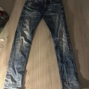 Säljer ett par blå jeans från Smog i bra skick. De har en snygg tvättad look och är i storlek 28/32. Perfekta för vardagsbruk med en klassisk stil. Det finns ett litet hål där bältet går igenom som ni ser på bilden går nog att fixa ganska lätt om man har tiden. Finns några små skavanker men inga jätte stora förutom hålet på bilden