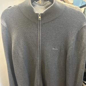 Grå stickad tröja från GANT - Säljer en stilren grå stickad tröja från GANT. Den har en dragkedja framtill och en hög krage som håller dig varm.