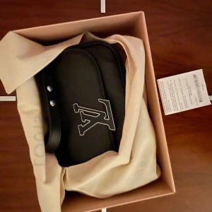 Svart axelväska från Louis Vuitton - Elegant svart axelväska från Louis Vuitton med det ikoniska LV-emblemet på framsidan. Väskan har en stilren design med en justerbar axelrem och är tillverkad i ett slitstarkt material.